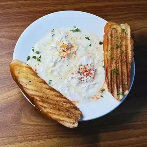 Turkish Eggs Çılbır with poached eggs, creamy yogurt, and paprika drizzle on plate